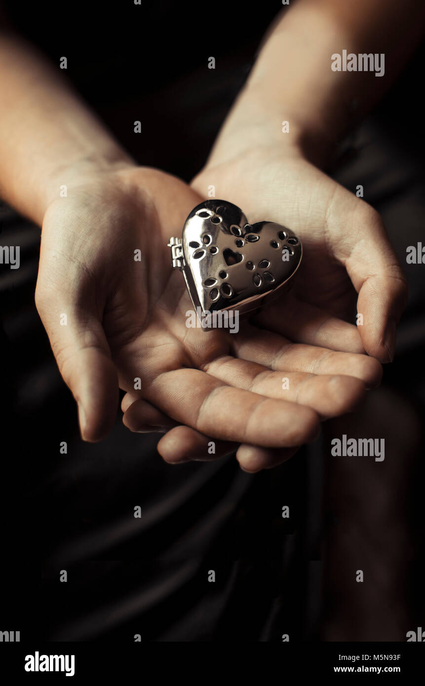 hands holding a heart shaped silver box Stock Photo