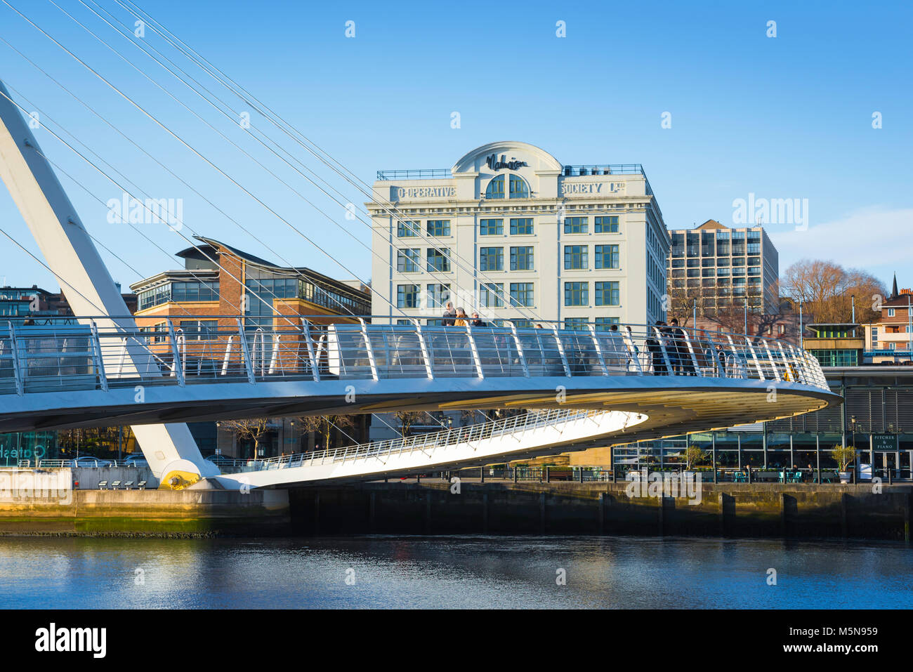 View of young people walking across the Millennium Bridge with the Quayside area of the city of Newcastle upon Tyne in the background, England, UK Stock Photo