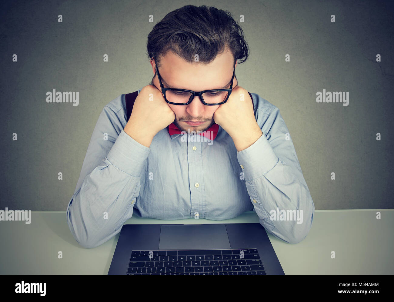 Bored business man with no motivation sitting at desk with laptop computer Stock Photo