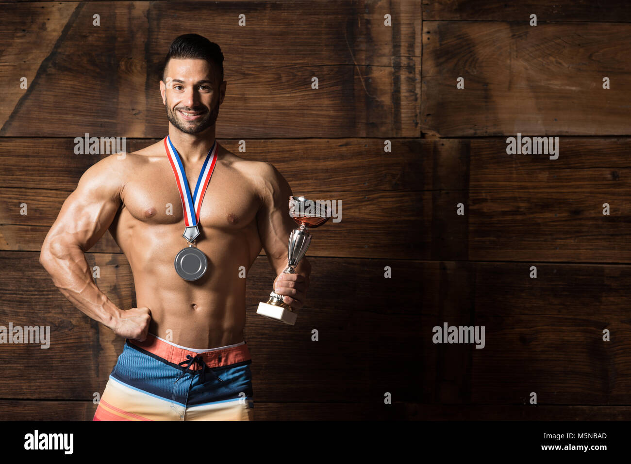 Bodybuilder Medals Bodybuilder Competitor Showing His Winning Medal Against a Wooden Wall ...