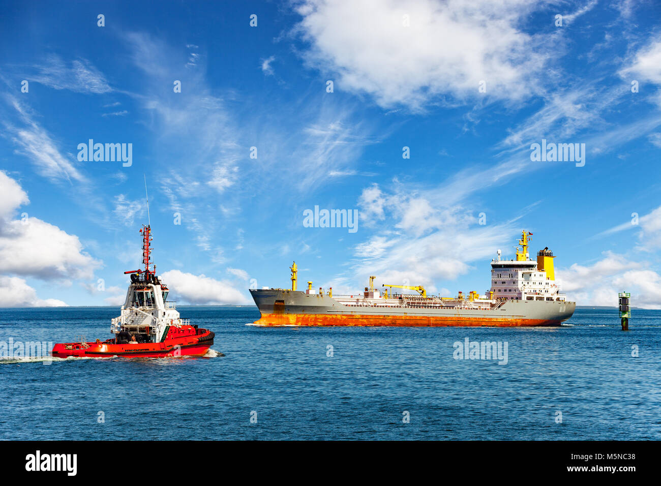 Red tug boat approaching to assist tanker. Stock Photo