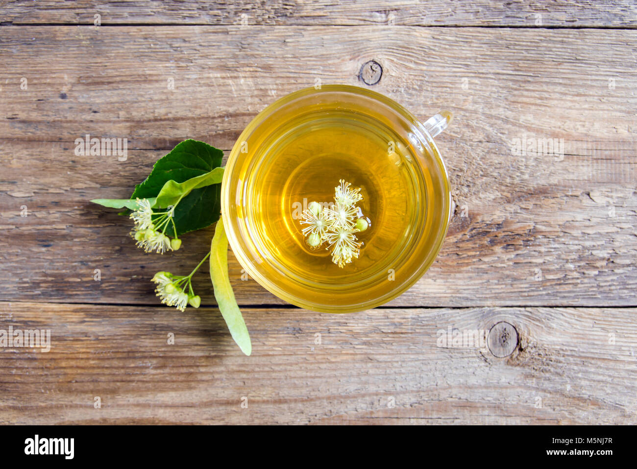 Healthy herbal linden tea with bunch of fresh linden flowers on wooden