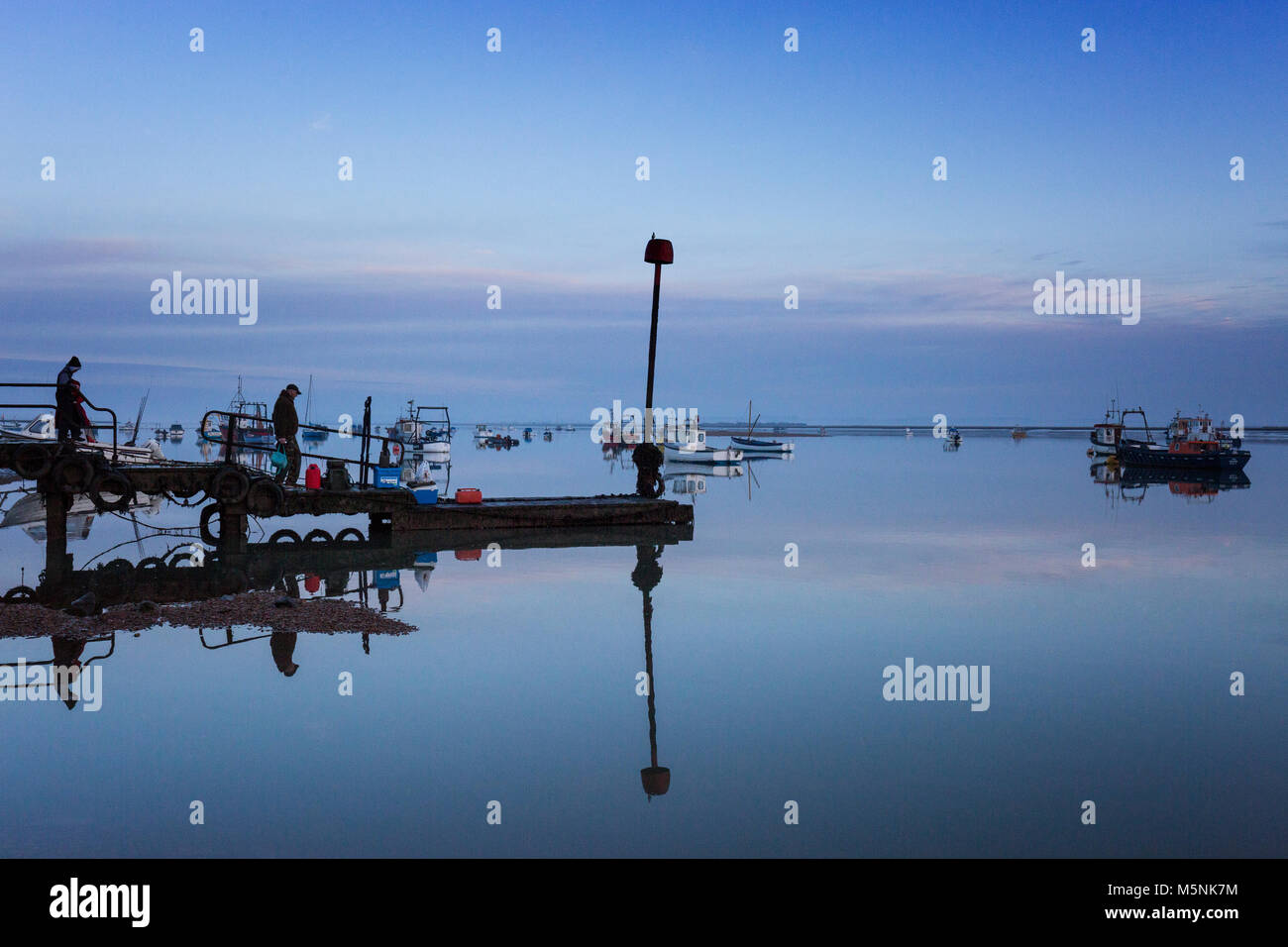 Two fisherman waiting for the boat to collect them from the jetty at Felixstowe Ferry in Suffolk, England. Stock Photo