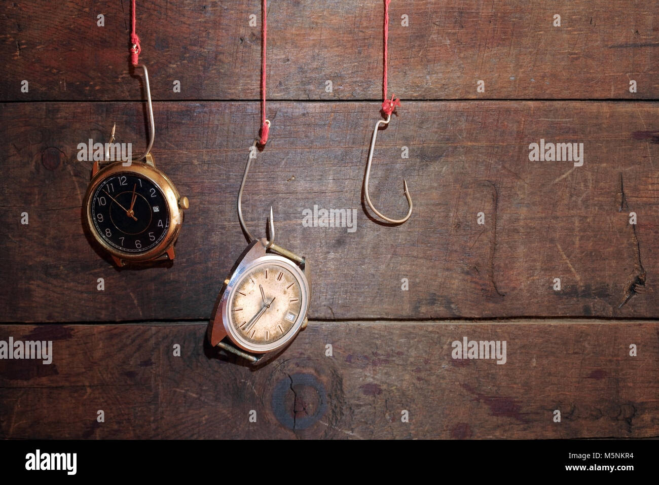 Two old watches hanging on fish hooks on wooden background Stock Photo