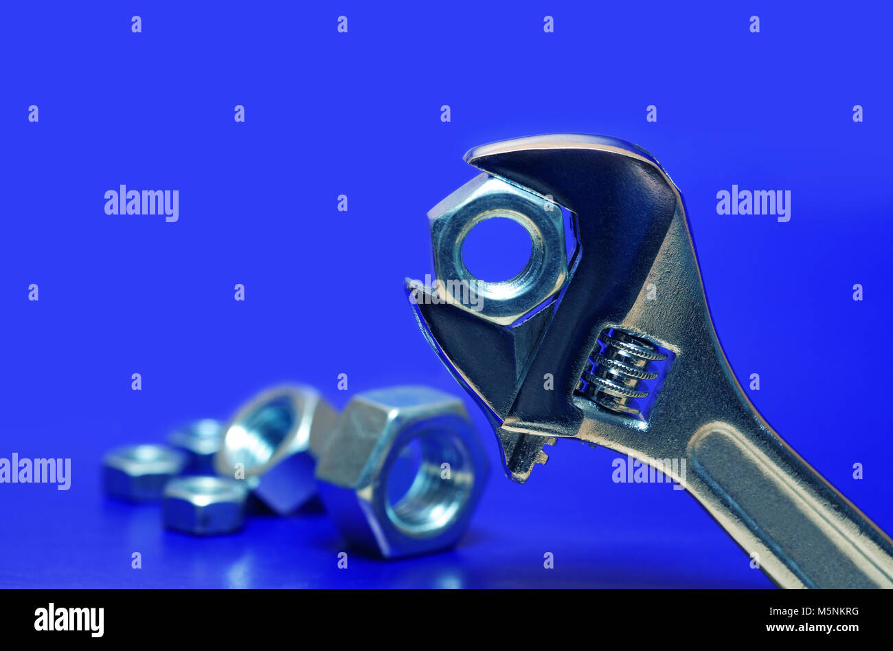 Extreme closeup of adjustable wrench gripping a screw nut on blue