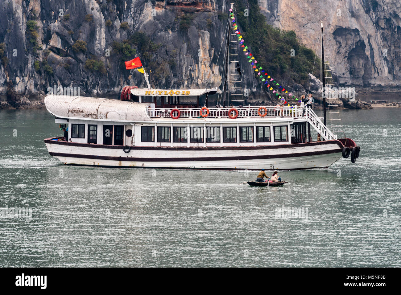 Tourist passenger cruise ship sails ahead of two fishermen in a small rowing boat at Halong Bay, Vietnam Stock Photo