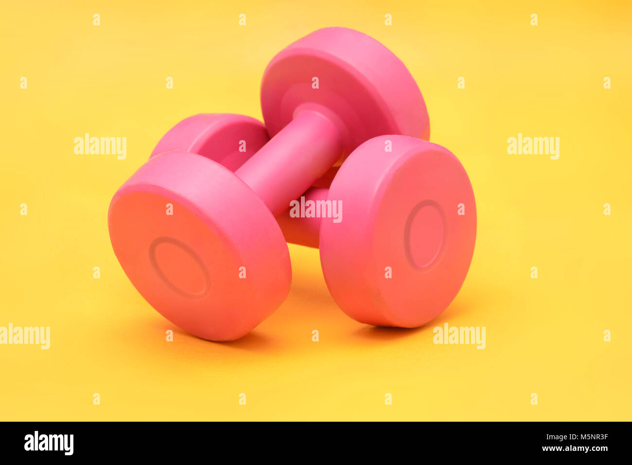Pink Dumbbells isolated on yellow background fitness concept Stock Photo