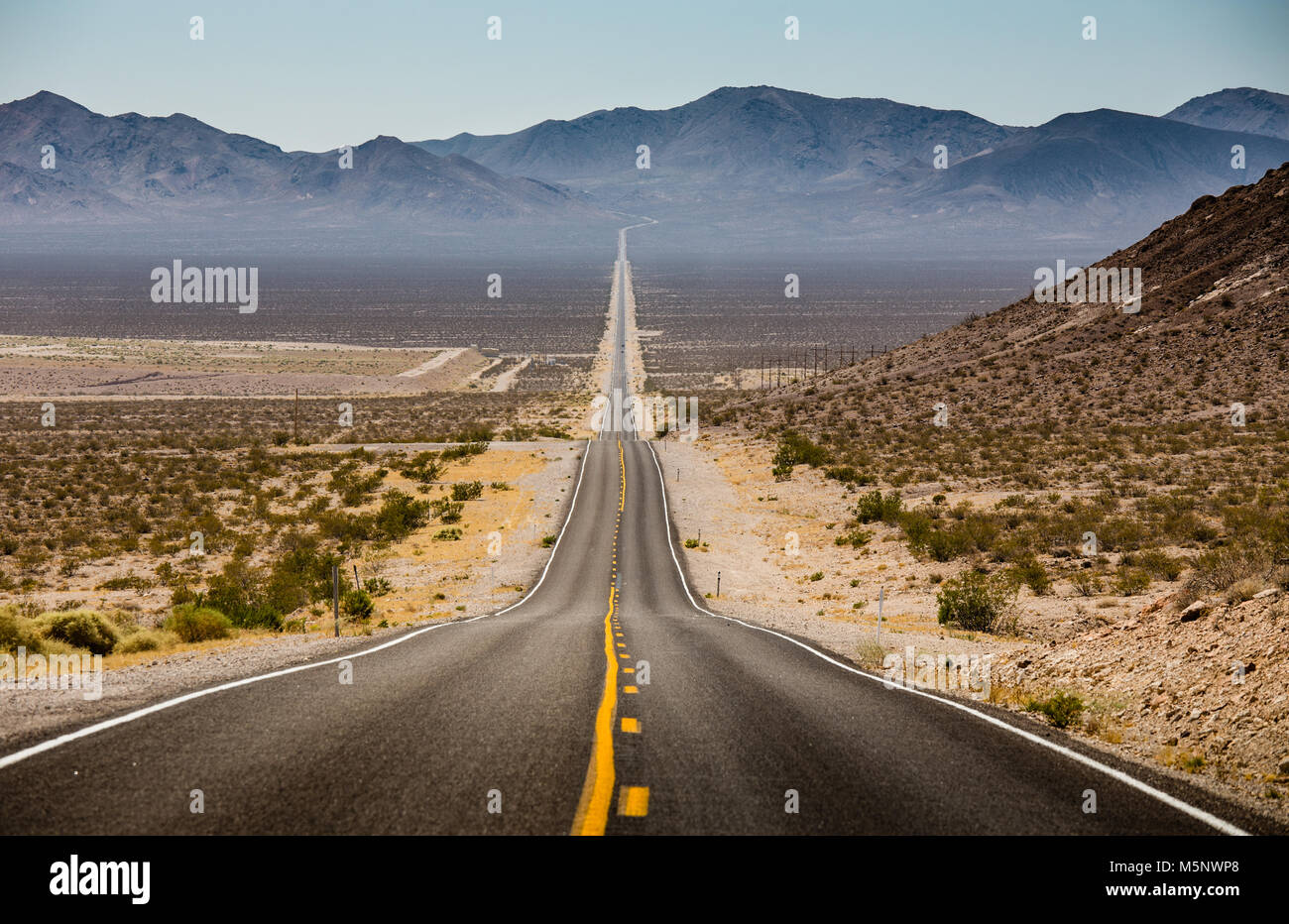 Classic panorama view of an endless straight road running through the barren scenery of the American Southwest with extreme heat haze on a beautiful s Stock Photo