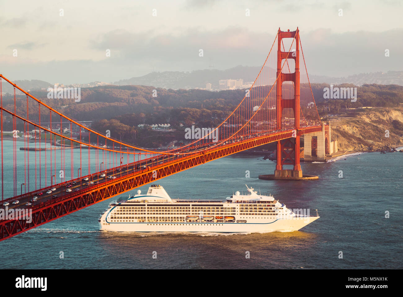 Cruise ship passing famous Golden Gate Bridge with the skyline of San Francisco in the background in golden evening light at sunset, California, USA Stock Photo