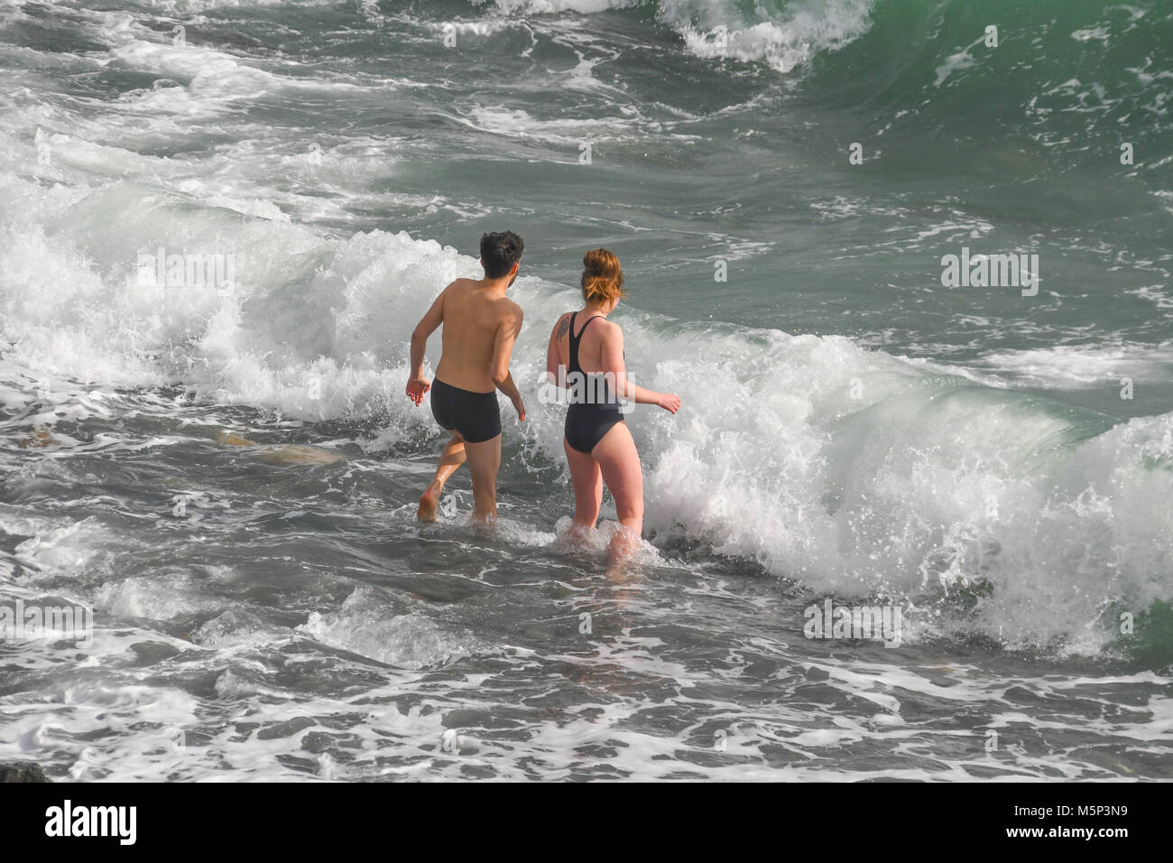 Mousehole, Cornwall, UK. 25th Feb 2018. UK Weather. Sunday was a freezing cold day in Cornwall, with strong winds from the 'beast in the east'. Neverthless this hardy couple decided to strip off and go for a invigorating paddle in the sea. Credit: cwallpix/Alamy Live News Stock Photo