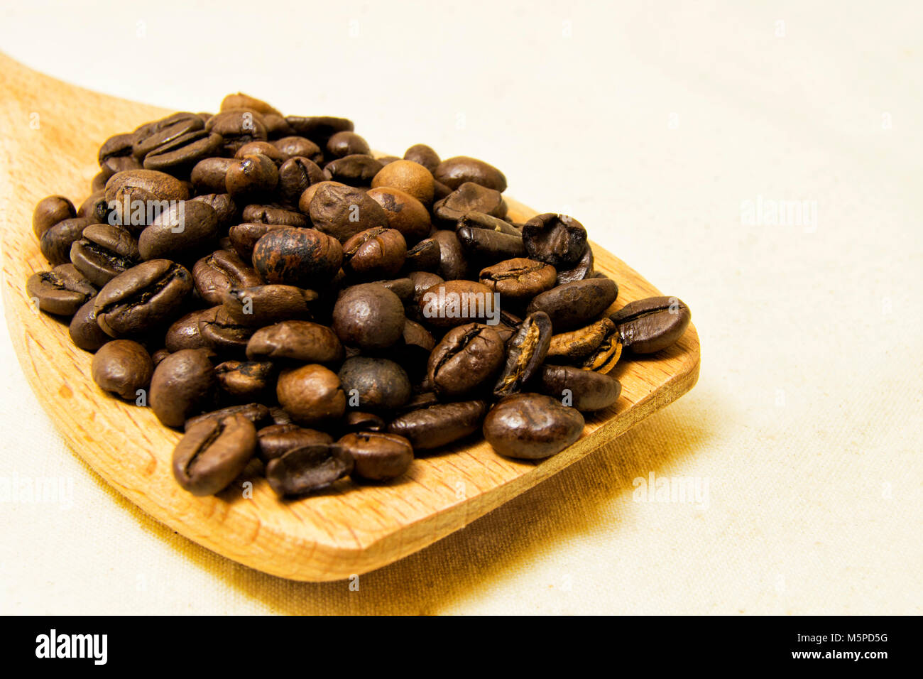 close up of roasted coffee beans on a wood spoon with white background ...