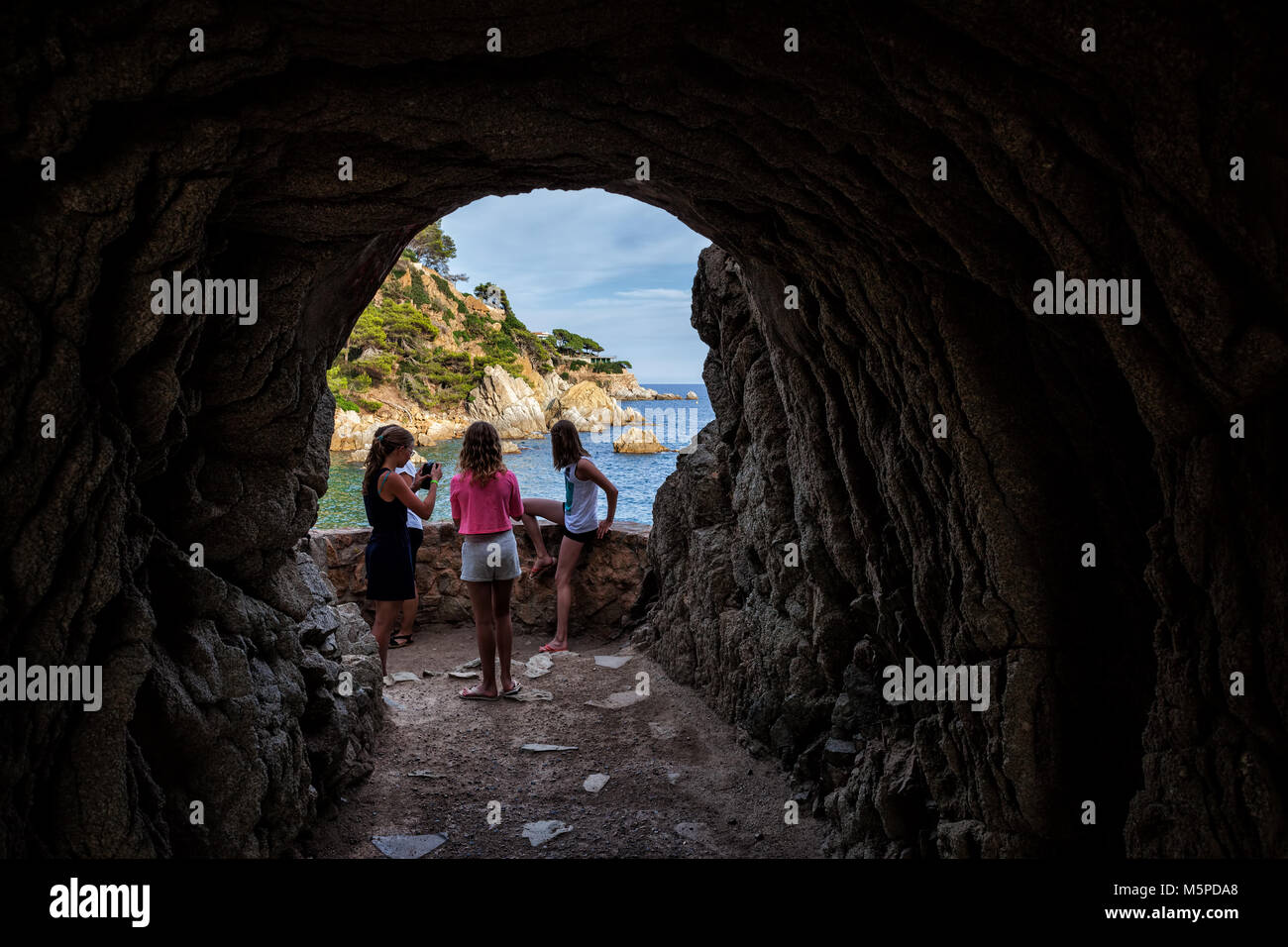 Coastal cave below the cliff, adventure travel scenery, young girls looking to the sea, Lloret de Mar, Costa Brava, Catalonia, Spain, Europe Stock Photo