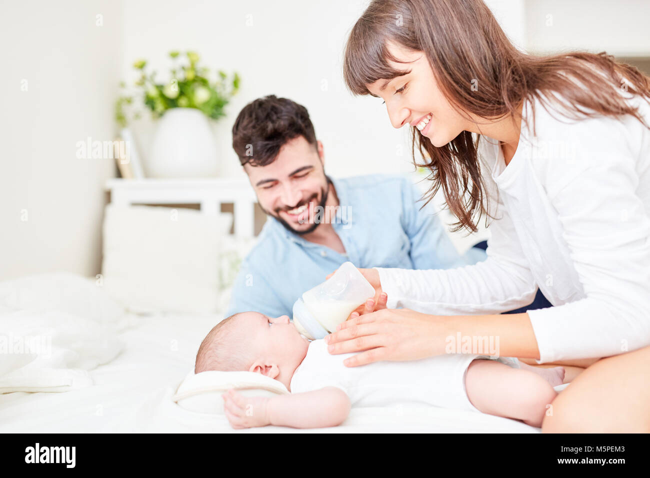 Happy parents as mother and father together feed their baby with milk Stock Photo