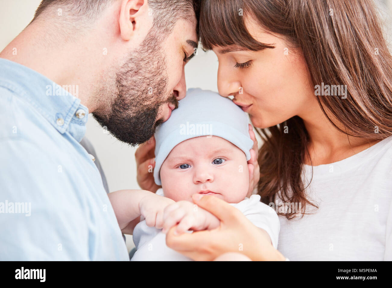 Mother and father together kiss their baby on the forehead Stock Photo