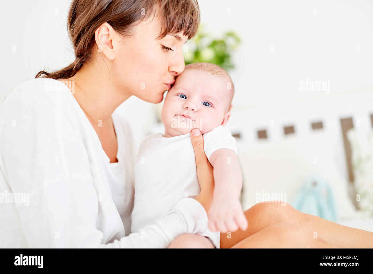 Affectionate mother tenderly kisses her forehead from her infant at home Stock Photo