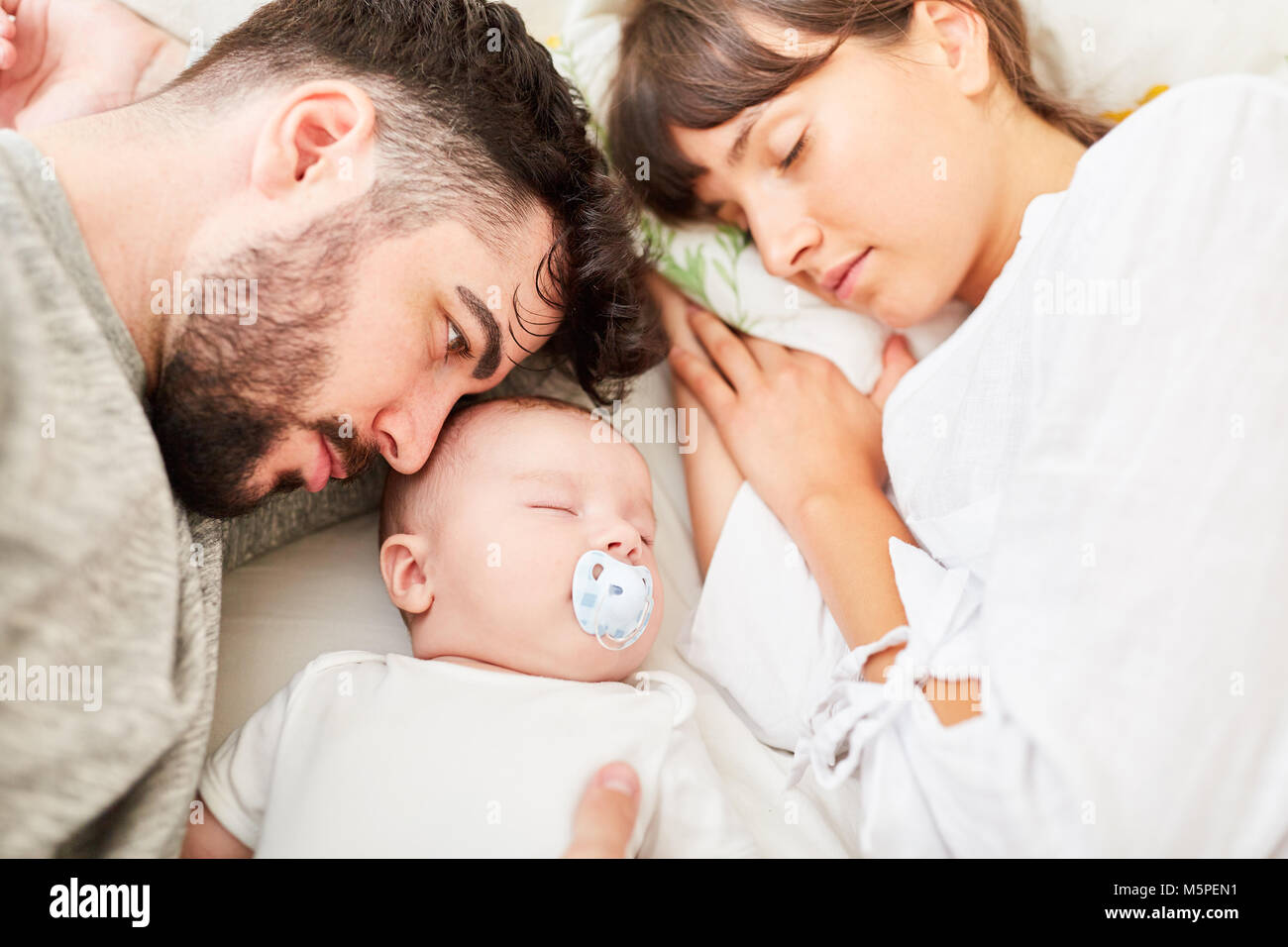 Father and mother as caring parents lie relaxed with baby on the bed Stock Photo
