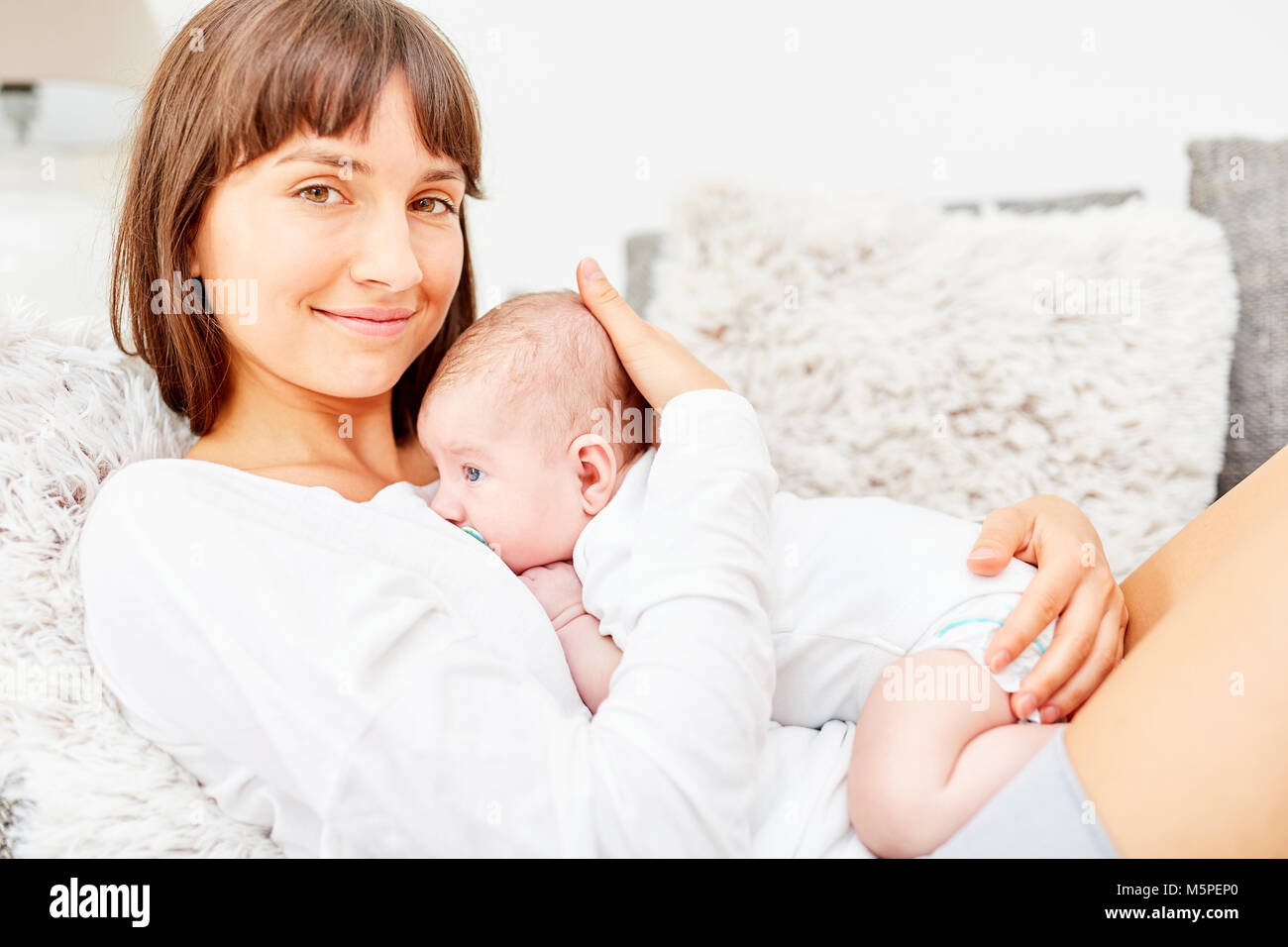 Woman as a happy mother lies on the sofa with newborn baby in her arms Stock Photo