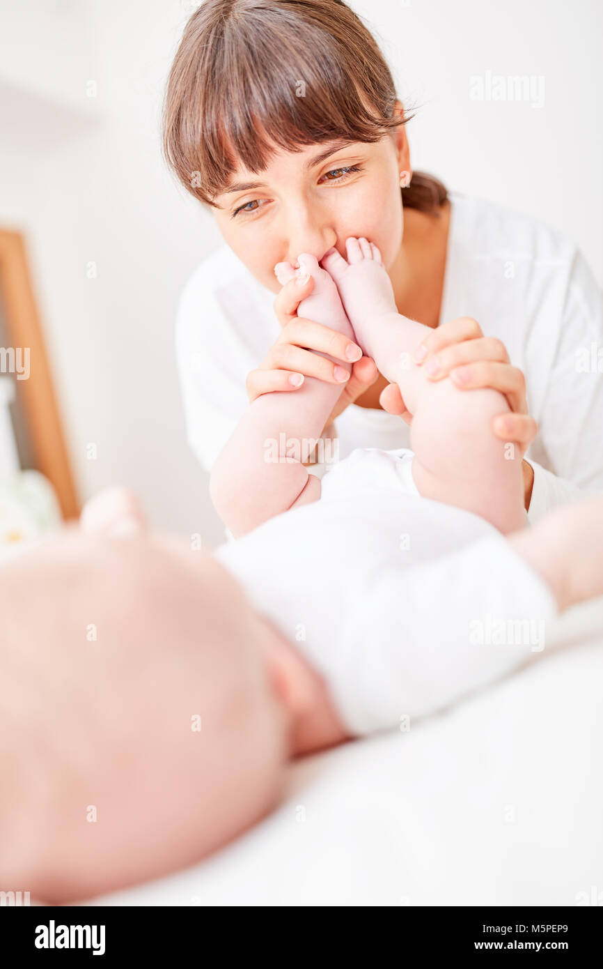 Woman as a happy mother lovingly kisses the feet of her newborn baby Stock Photo