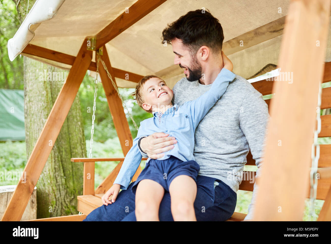 Boy is kidding with his father around on the garden swing in the garden Stock Photo