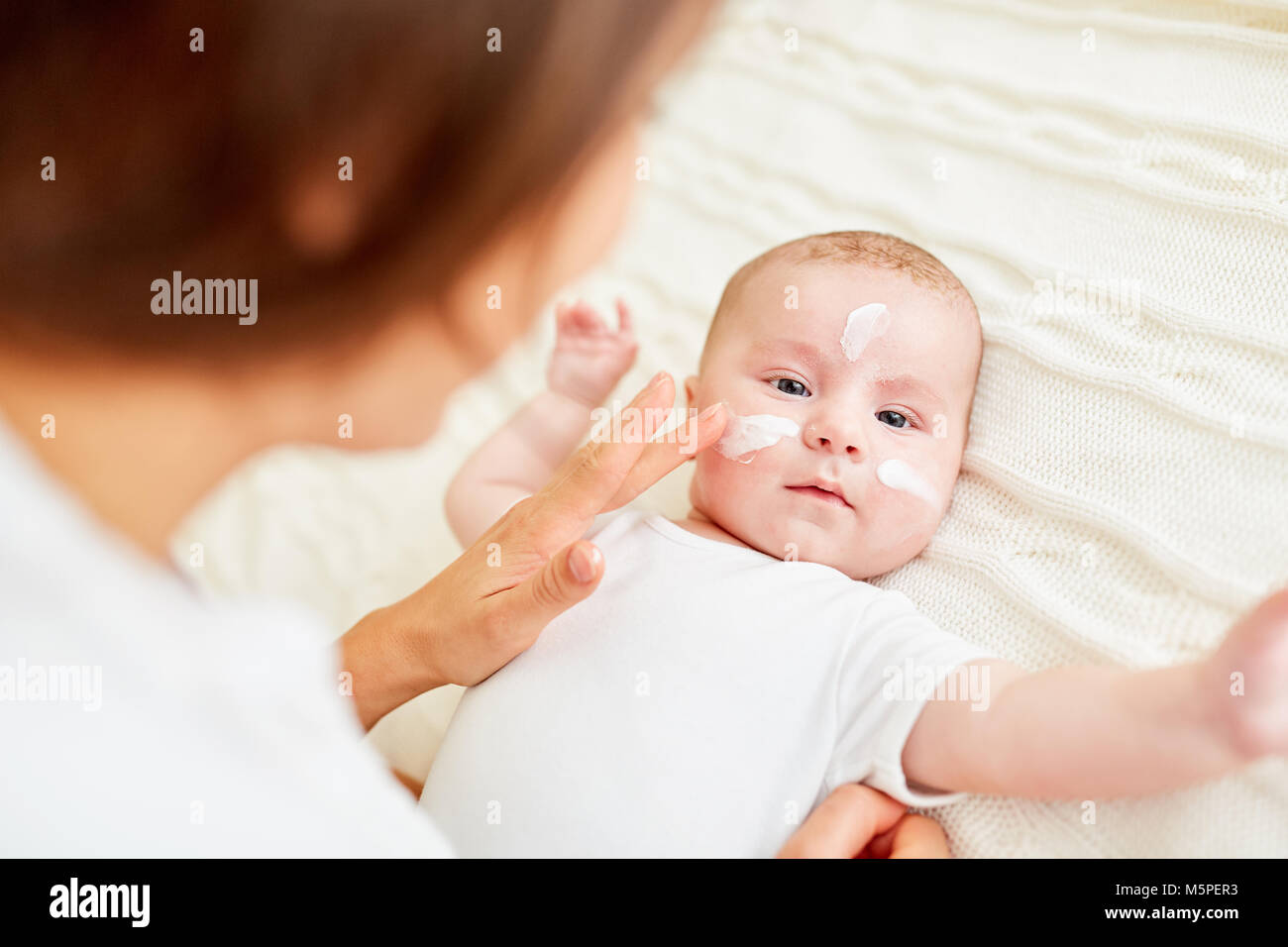 Young woman creams baby face to protect the baby skin as a baby care