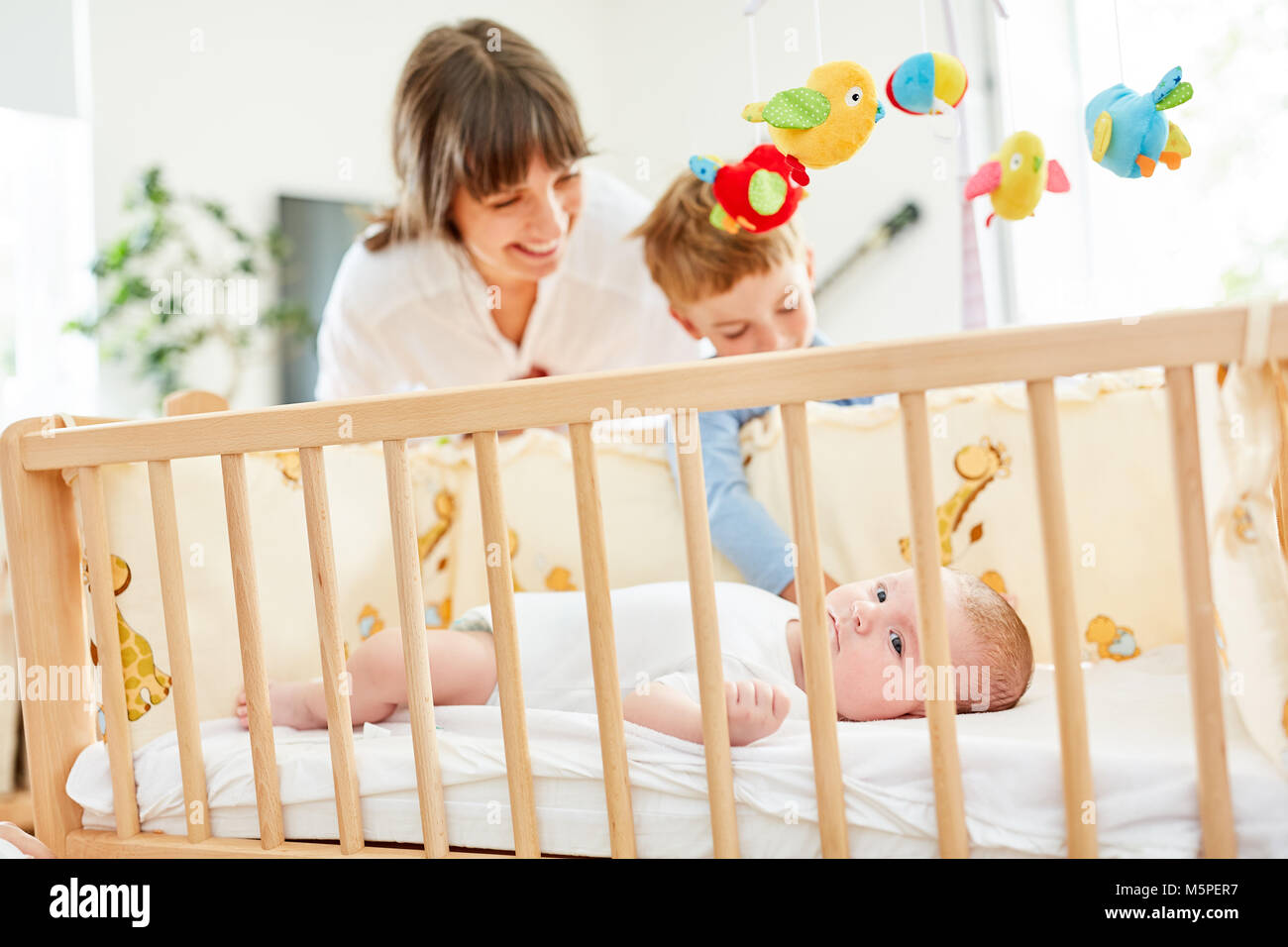 Mother and brother at the baby bed look on newborn baby in the nursery Stock Photo