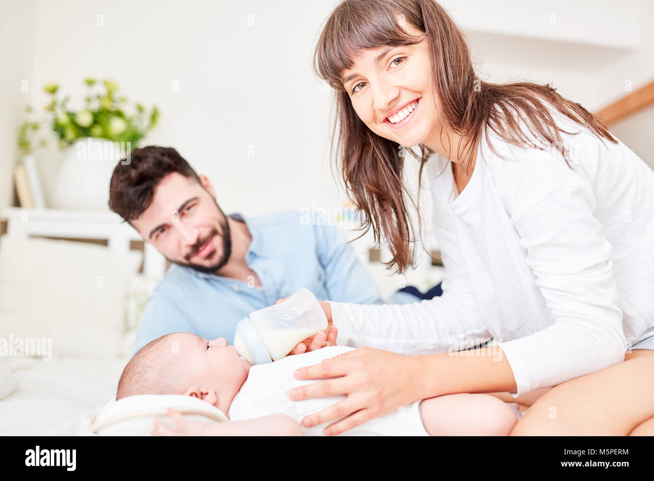 Mother and father as parents give the bottle of baby milk to their baby Stock Photo