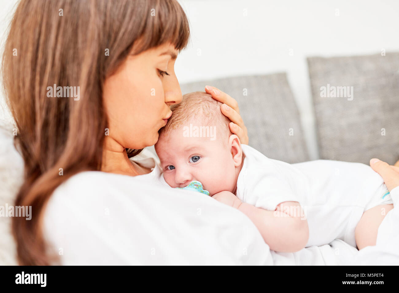 Happy mother lovingly kisses her baby on the forehead on the sofa at home Stock Photo