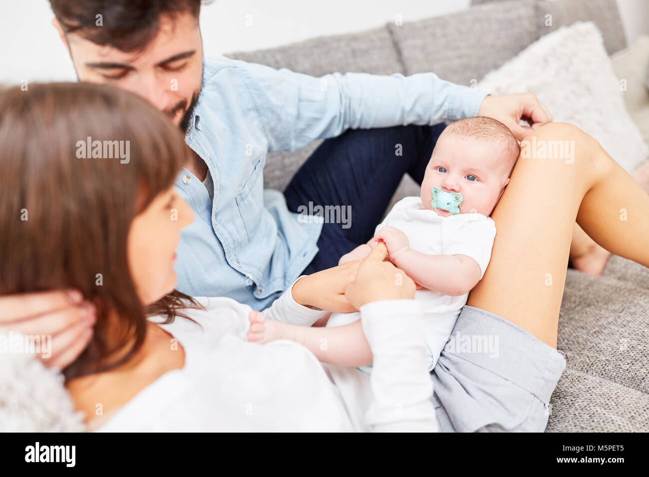 Happy parents and their newborn baby are sitting relaxed on the sofa Stock Photo