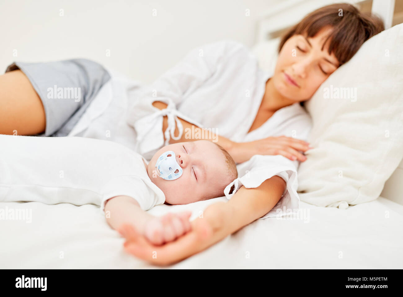 Mother and newborn baby sleep peacefully together on the bed Stock Photo