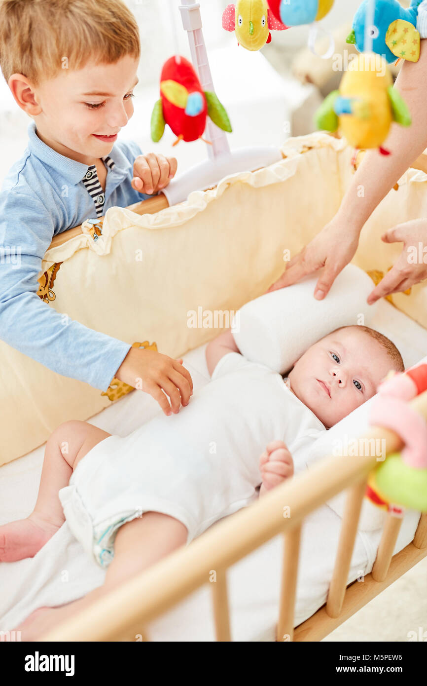 Smiling boy as brother looks on newborn baby in baby bed Stock Photo ...