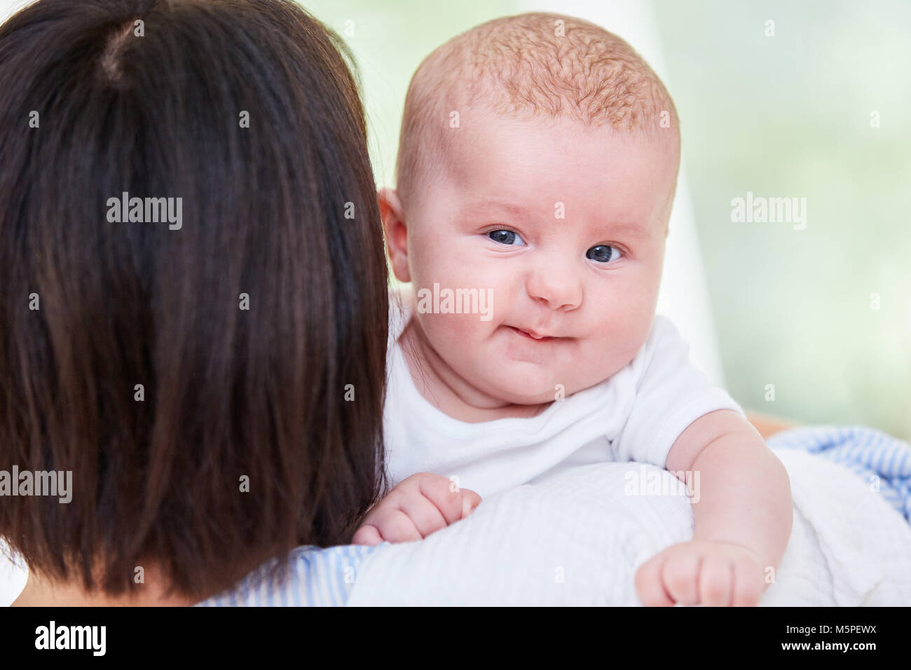 Newborn cute baby on mother's arms looks curious Stock Photo