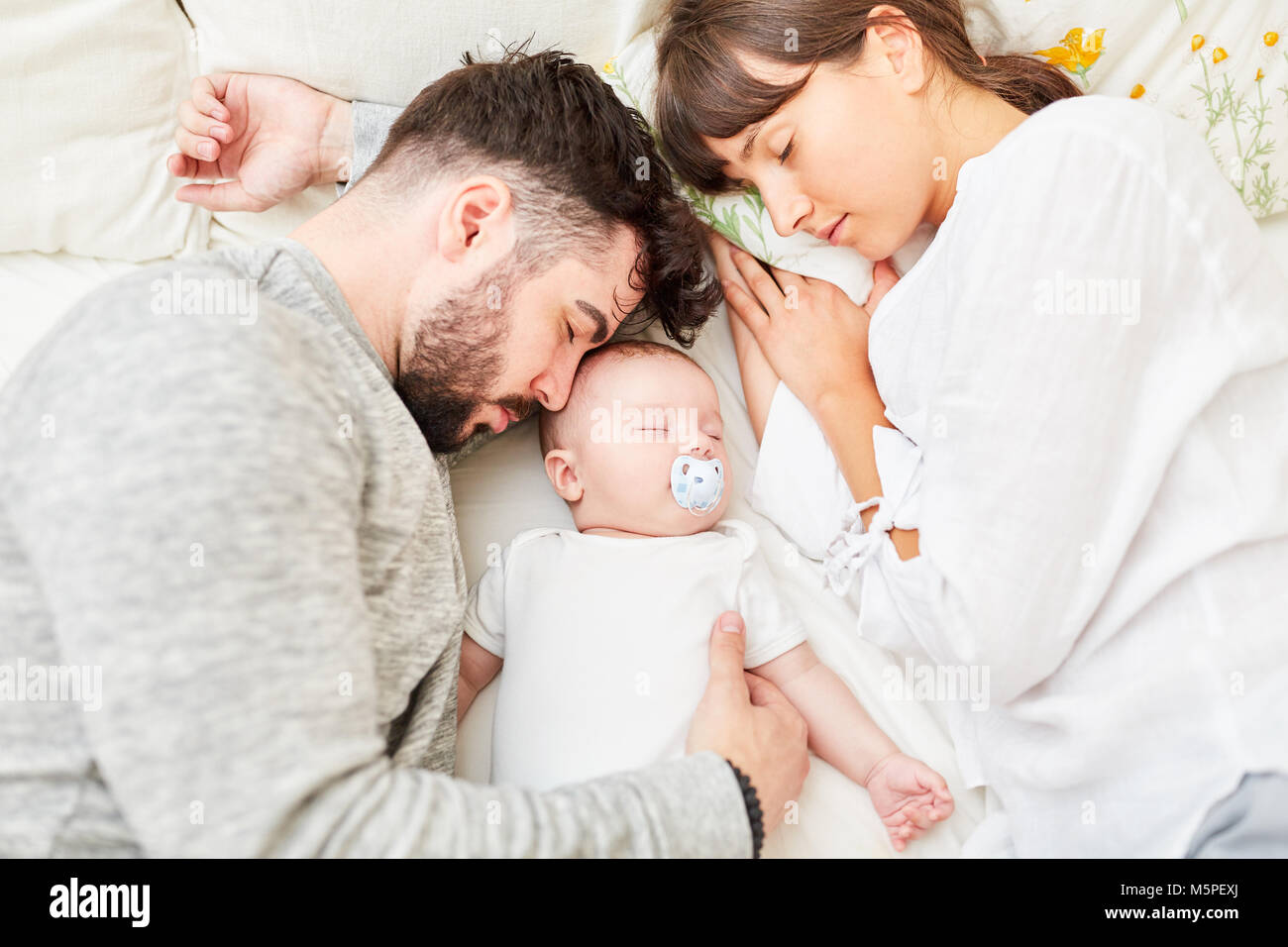 Mother and father as happy parents sleep next to their little baby Stock Photo