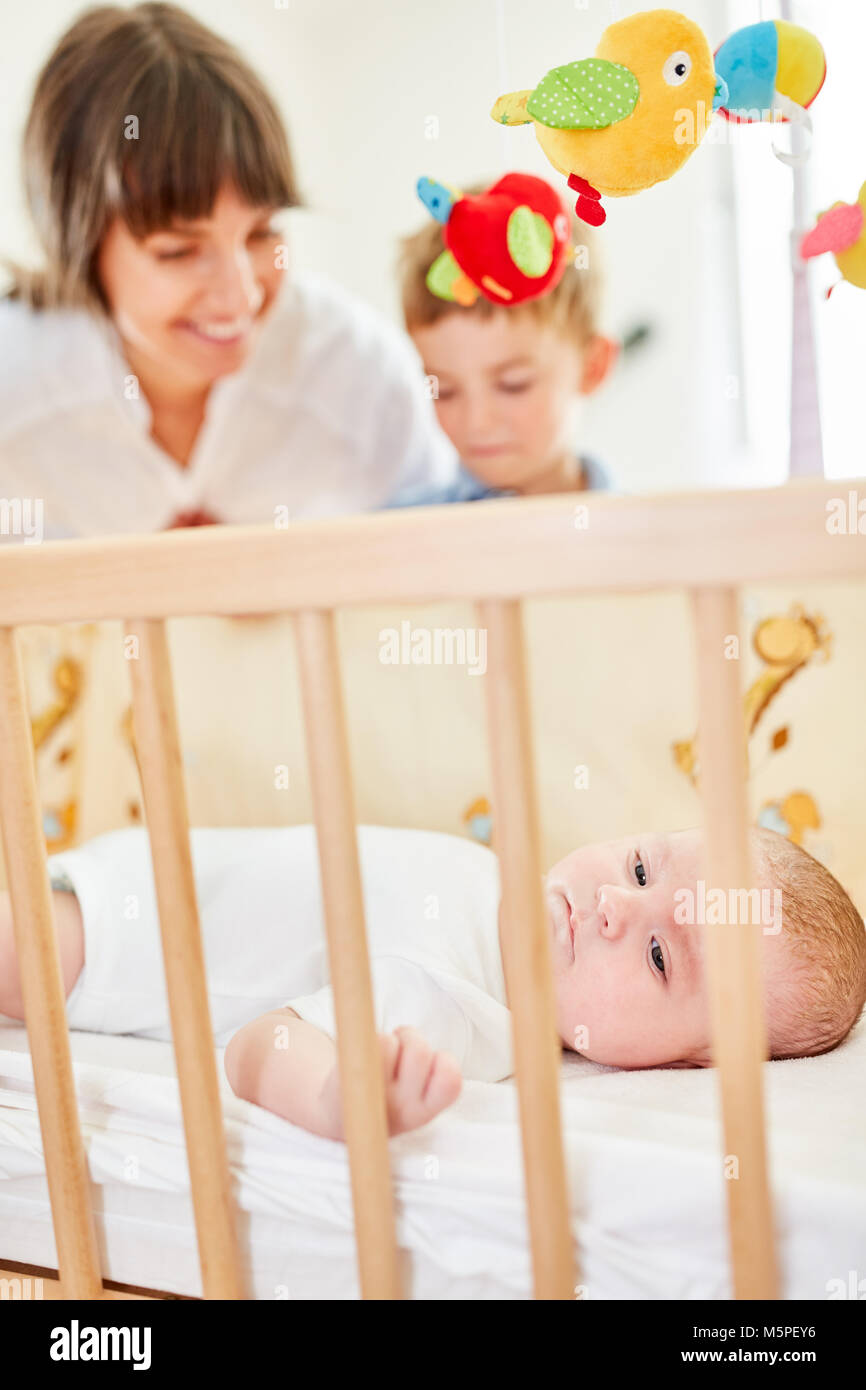 Newborn baby in baby bed with mother and brother in the background Stock Photo