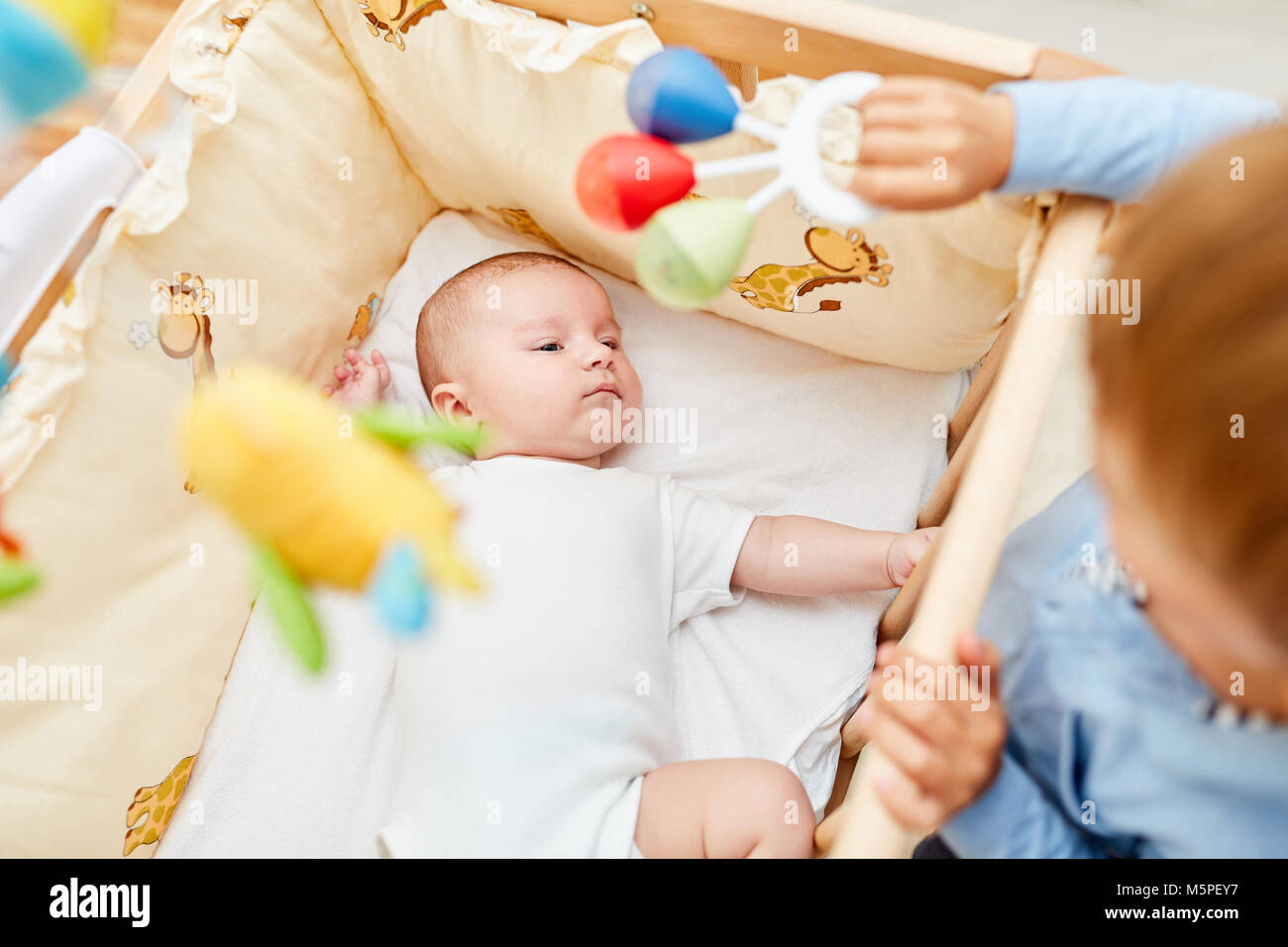 Boy looks at newborn baby while falling asleep in cot Stock Photo