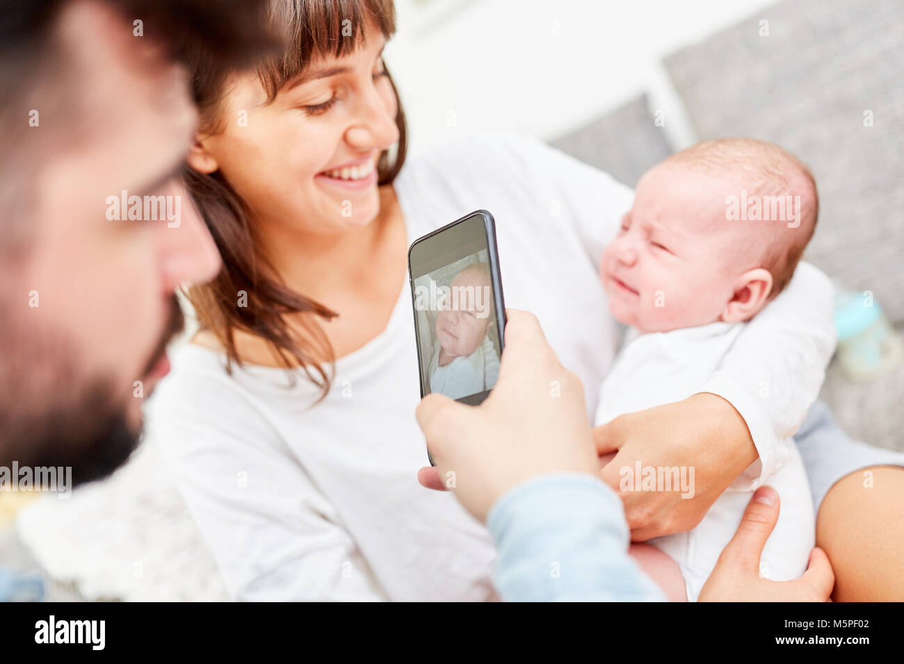 Father makes a photo of happy mother and baby with smartphone Stock Photo