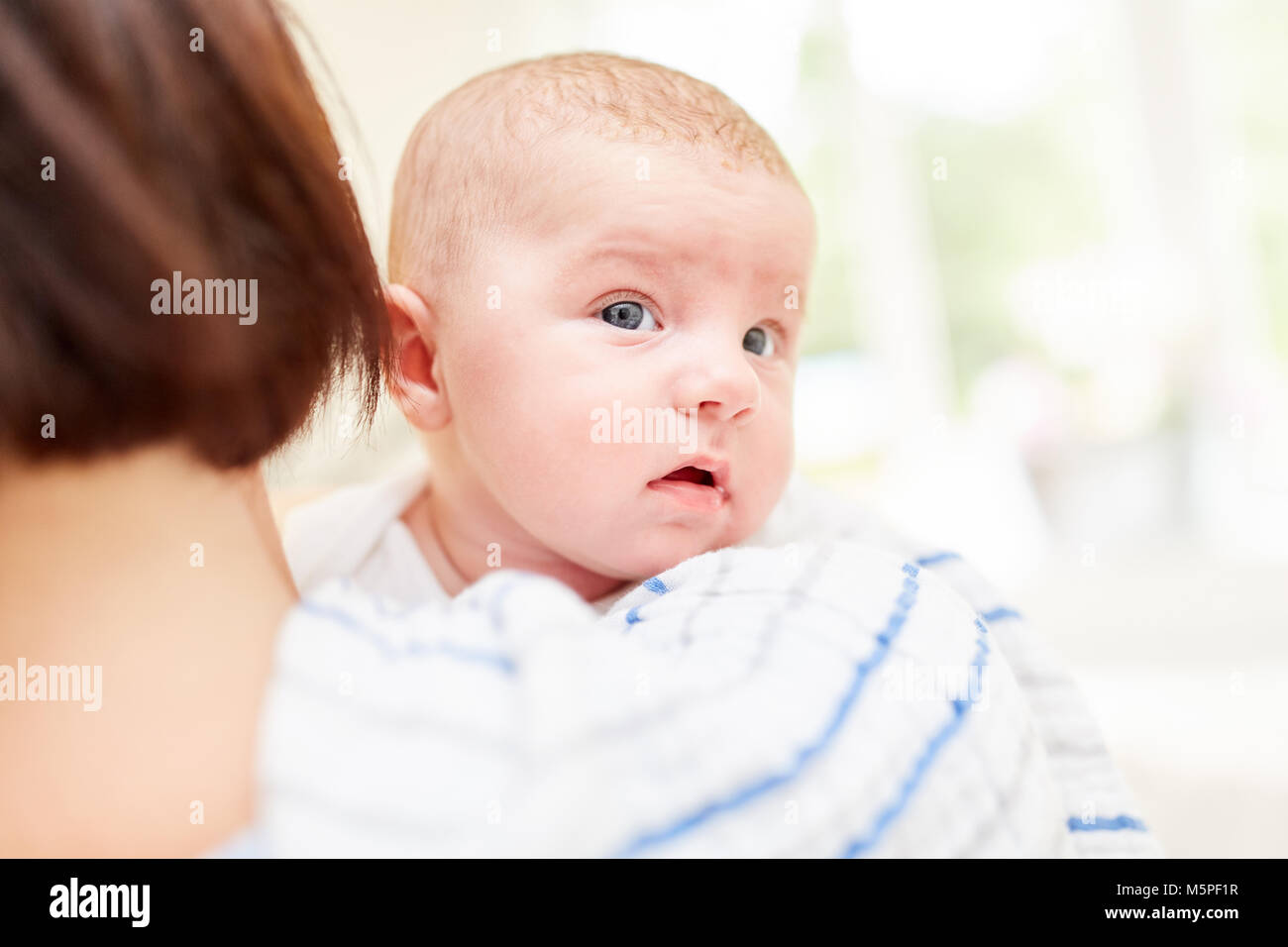 Newborn baby looks curiously at the mother's arms Stock Photo
