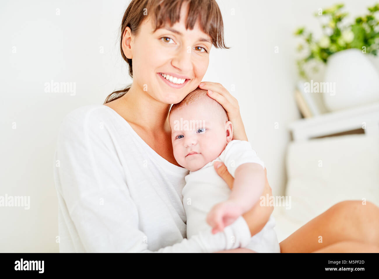 Happy young mother lovingly hugs her baby on the lap at home Stock Photo