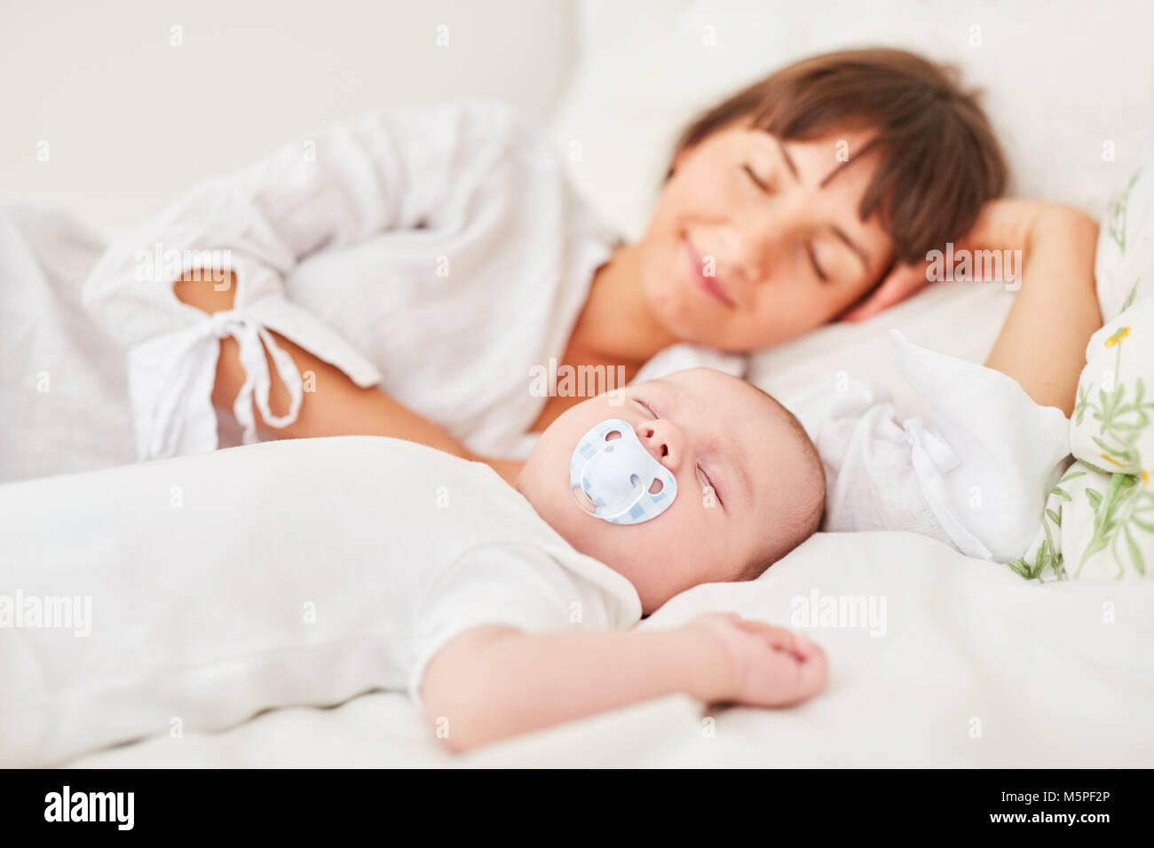 Mother and baby sleep peacefully together on the bed at home Stock Photo