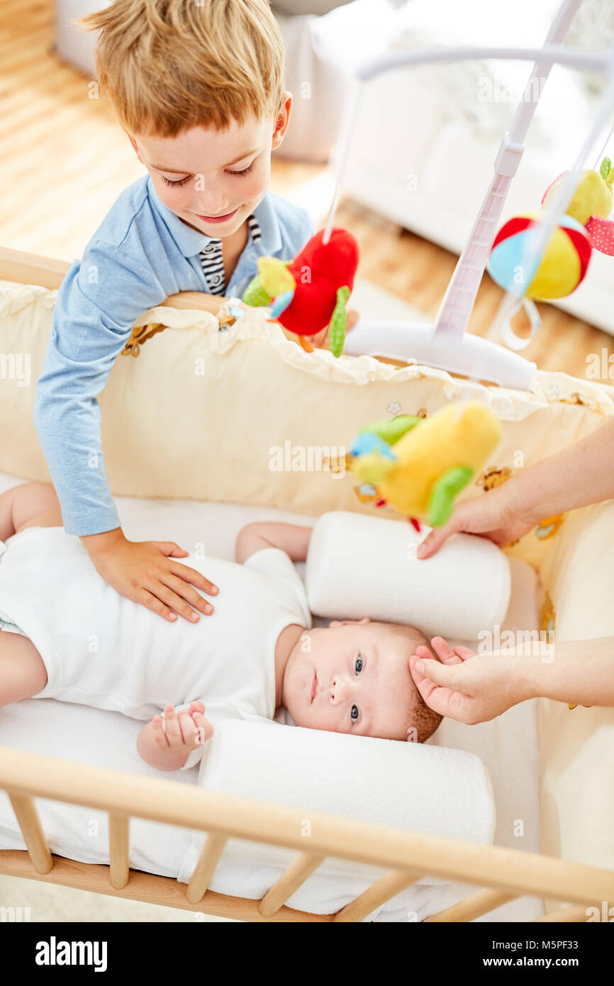 Young caring brother strokes newborn baby in baby cot Stock Photo