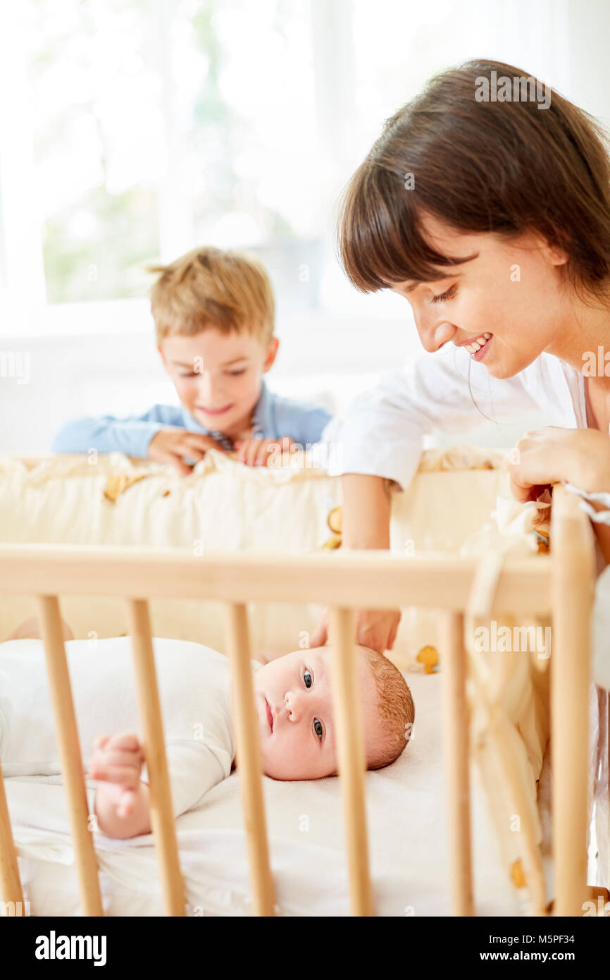 Happy mother and boy at baby bed watch baby falling asleep Stock Photo