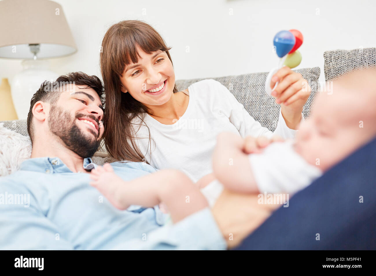Happy parents play with a rattle with their baby on the sofa Stock