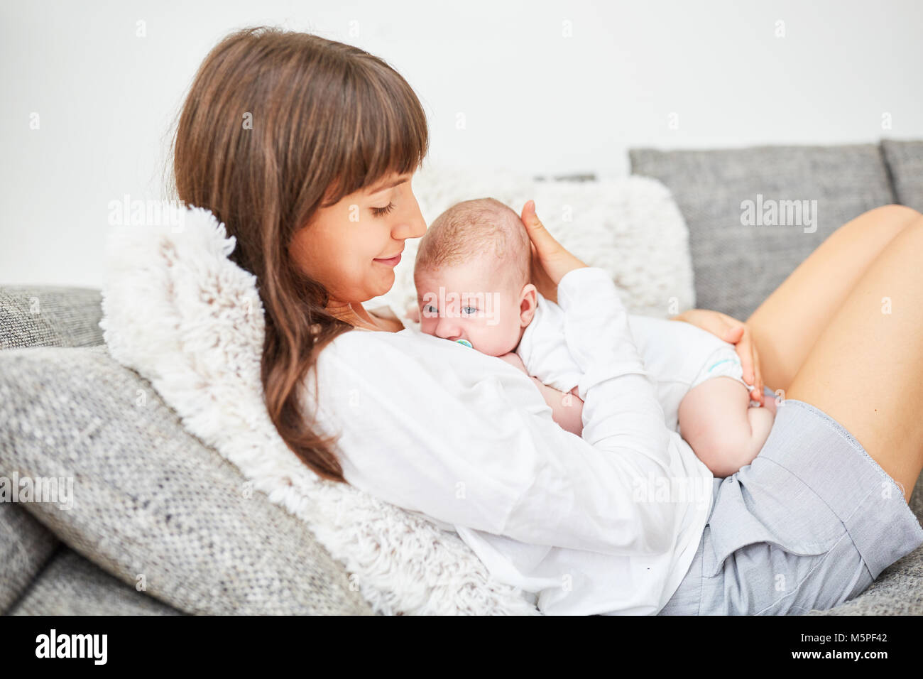 Mother lovingly cuddles with her newborn baby on the sofa Stock Photo