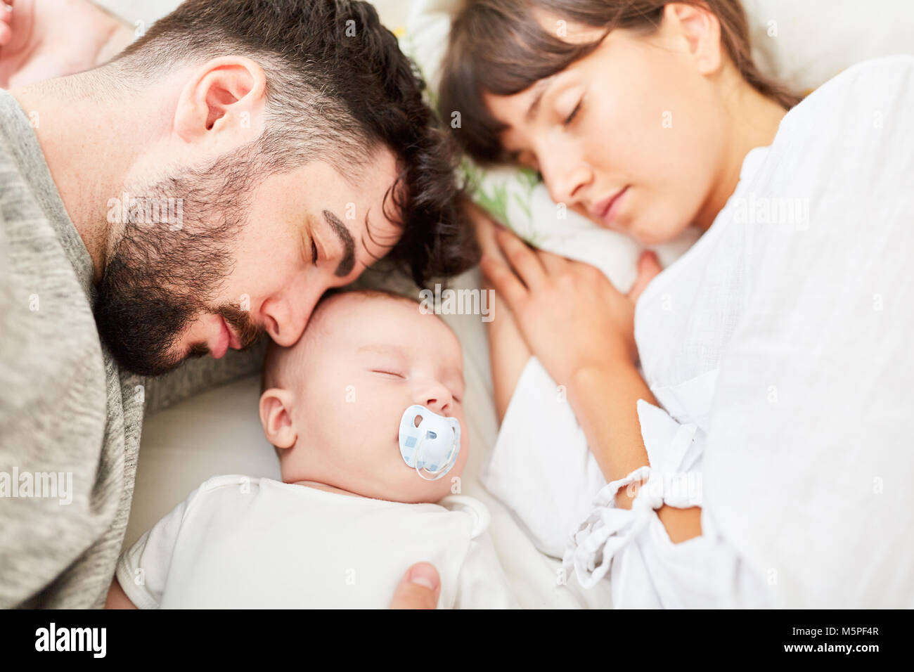 Sleeping parents and their little baby cuddle together relaxed Stock Photo
