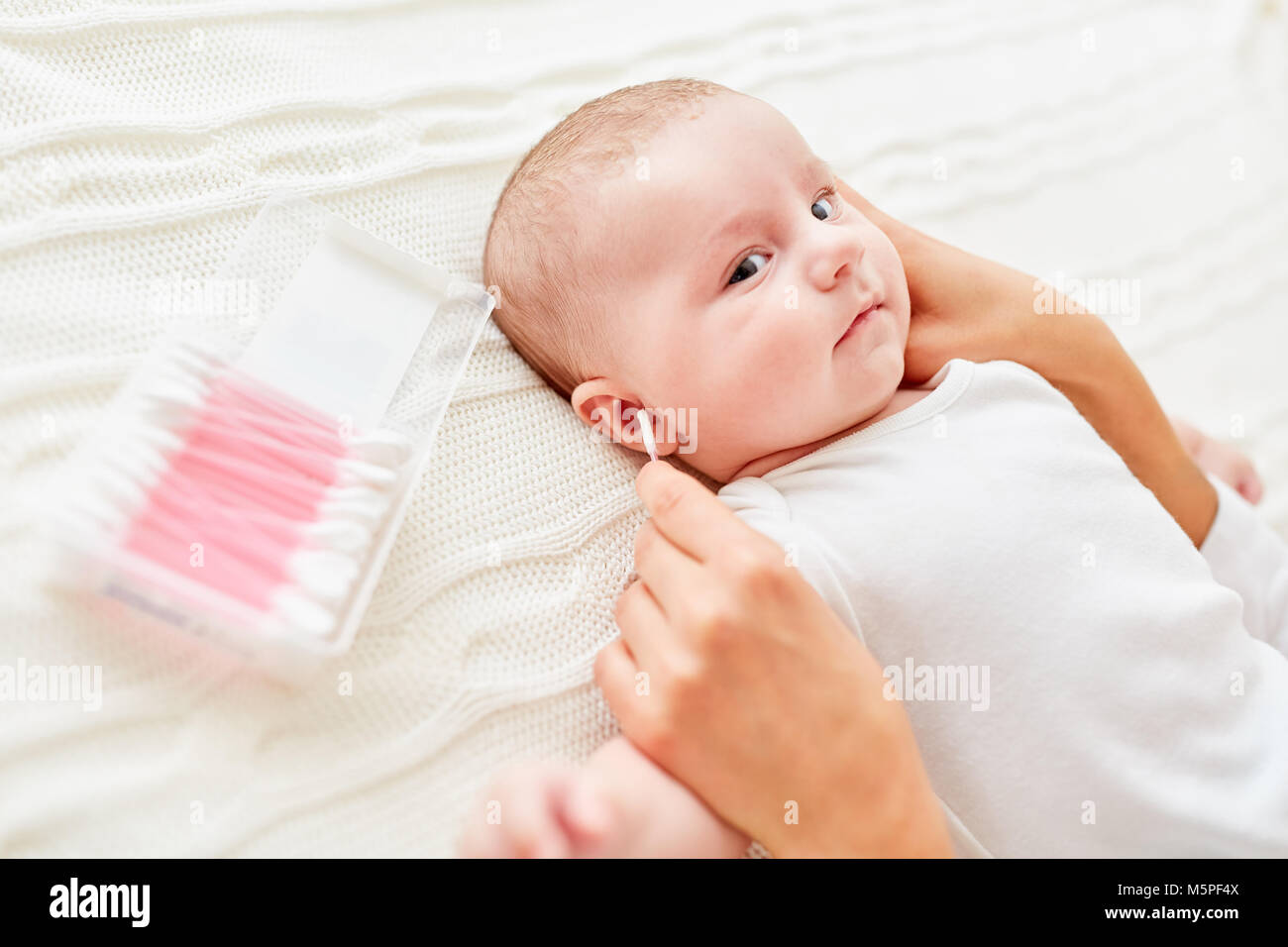 Hand cleans the ears of a baby with a cotton swab Stock Photo