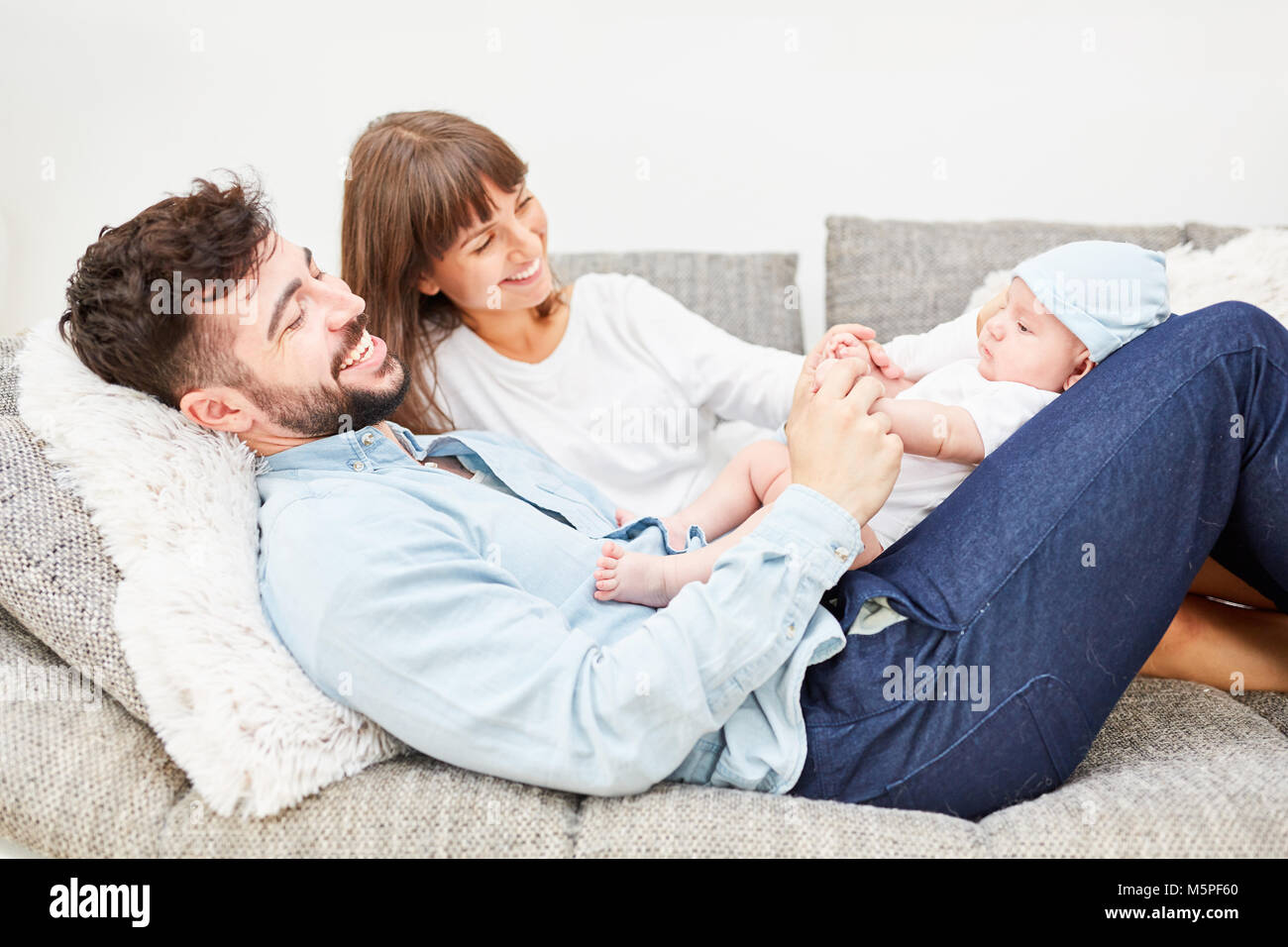 Father and mother as happy parents are lying on the sofa with their baby Stock Photo