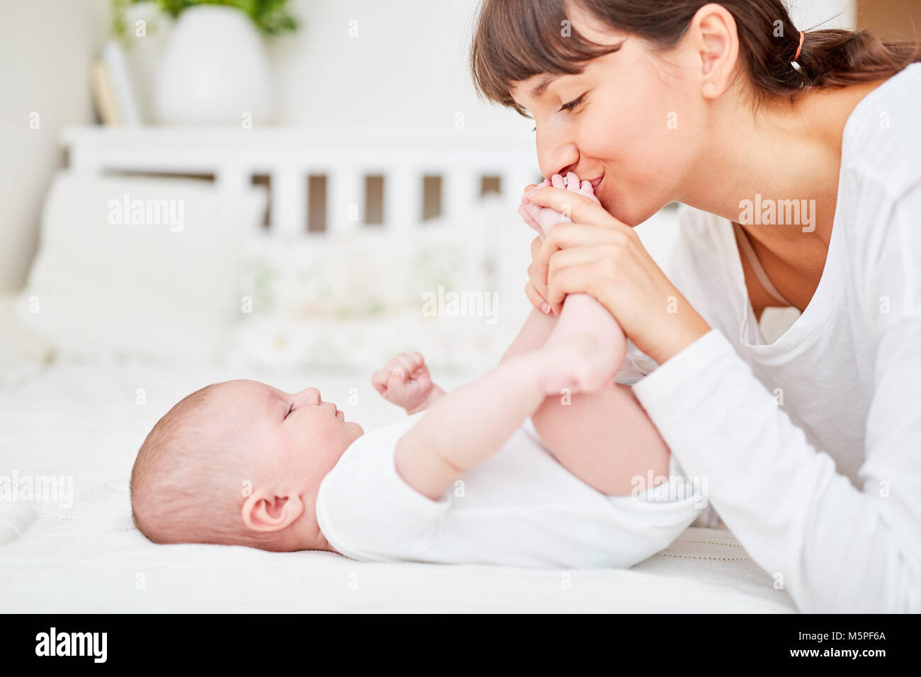Loving mother tenderly kisses the feet of her newborn baby Stock Photo