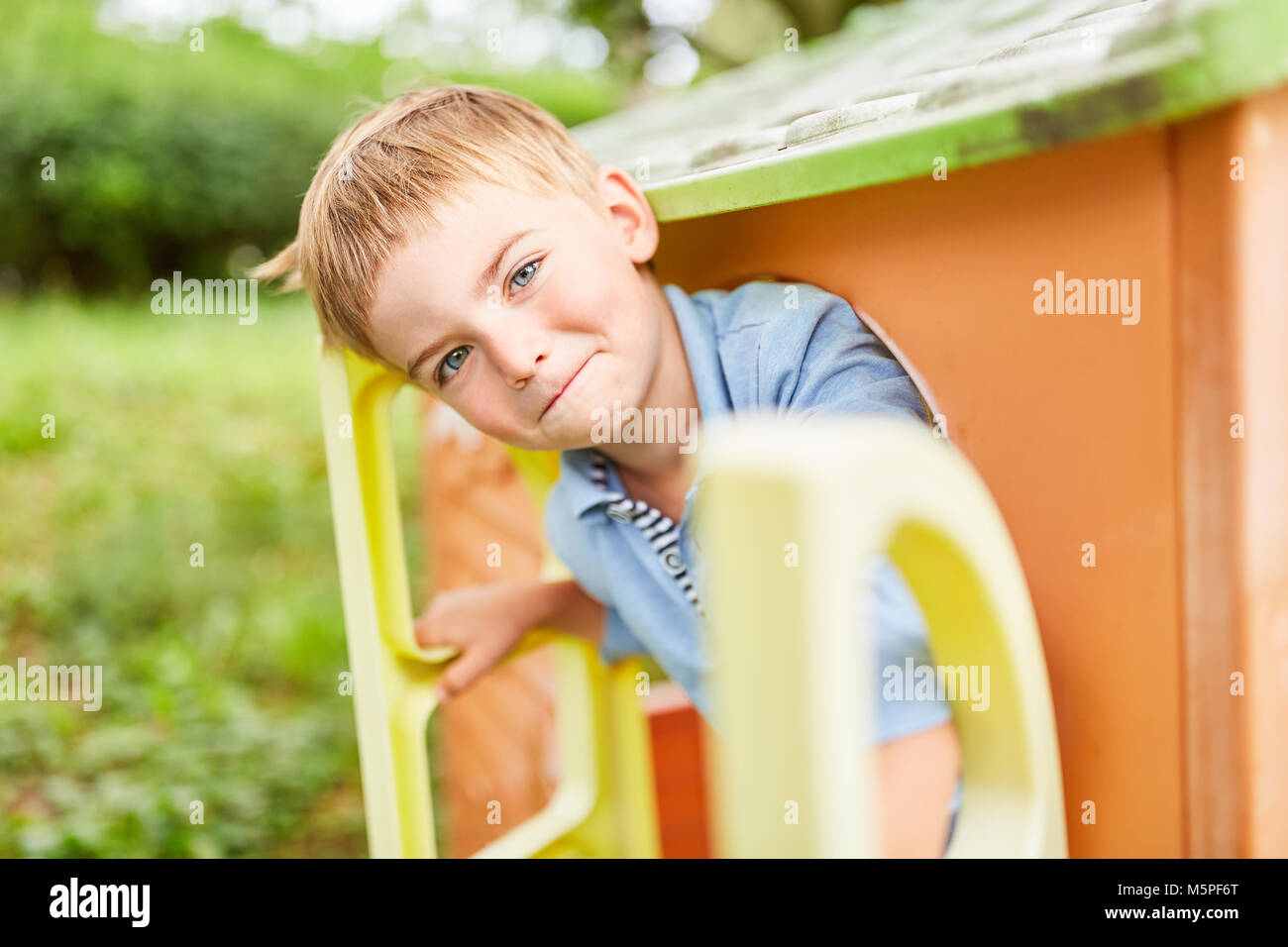 Boy smiles mischievously and looks out of the playhouse in the playground Stock Photo