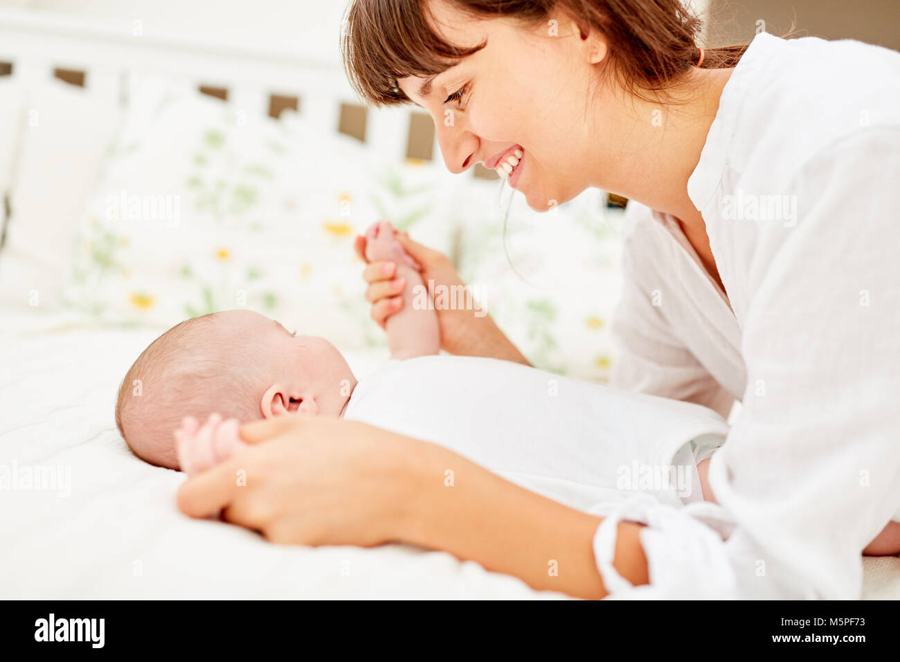 Young woman as a loving mother plays with her newborn baby Stock Photo