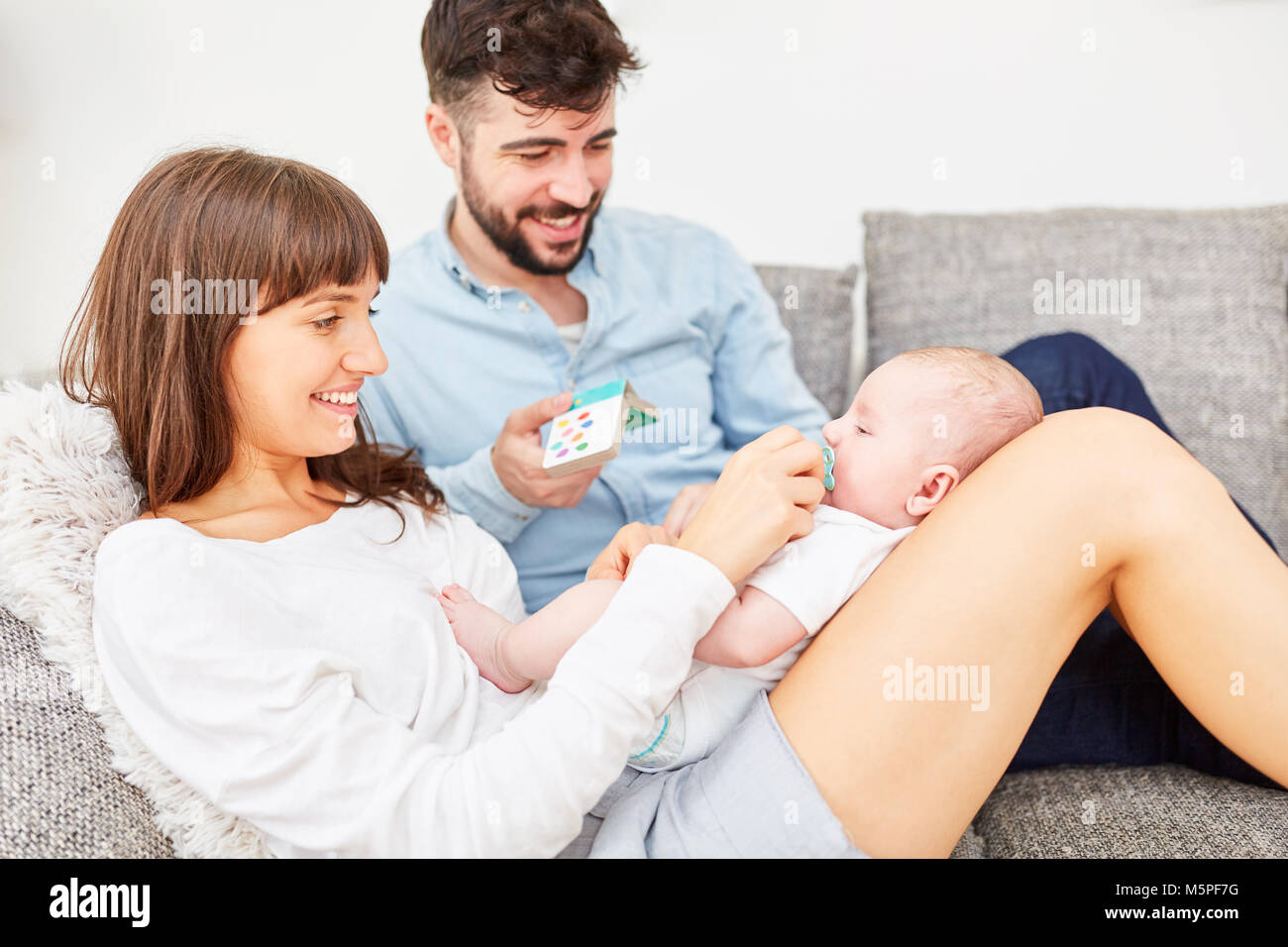Parents sit together with newborn baby on the sofa at home Stock Photo