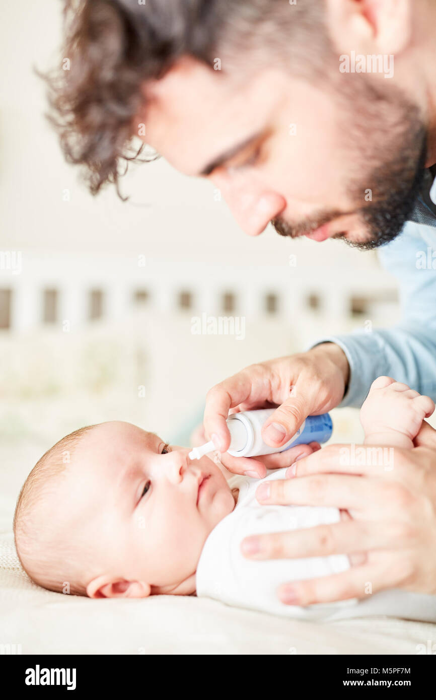 Sick baby gets nasal spray for cold from worried father Stock Photo